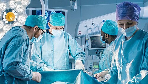 Several doctors and an assistant in an operating theatre with bluish light