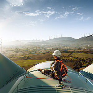 Ingénieur debout au sommet d'une éolienne et regardant un magnifique paysage au coucher du soleil.